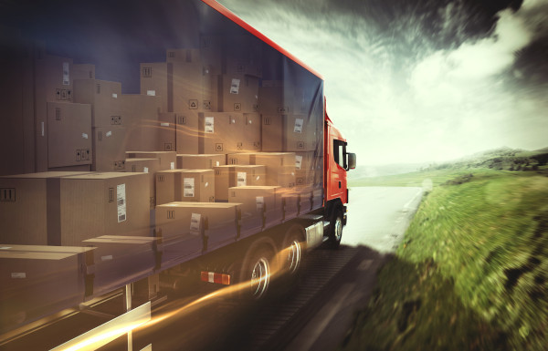 Semi-truck connected to a trailer with a translucent side showing the trailer is full of boxes