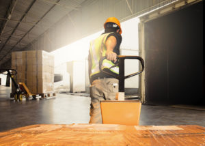 Warehouse worker unloading pallet shipment goods into a truck container